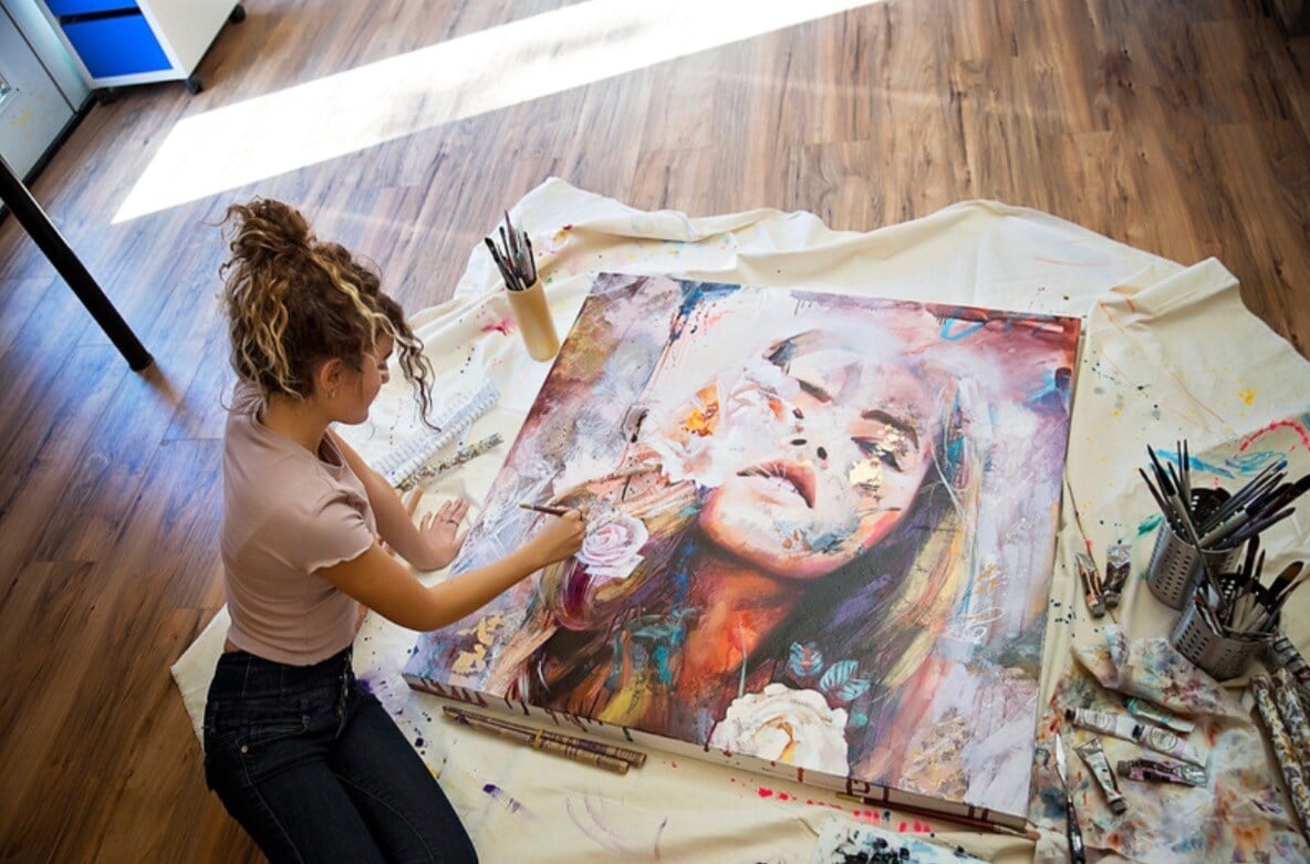 Damitra girl in tan shirt and black pants painting a portrait on the floor in well lit room